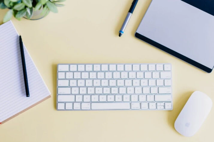 A yellow table with a keyboard, mouse, and notebook on top.