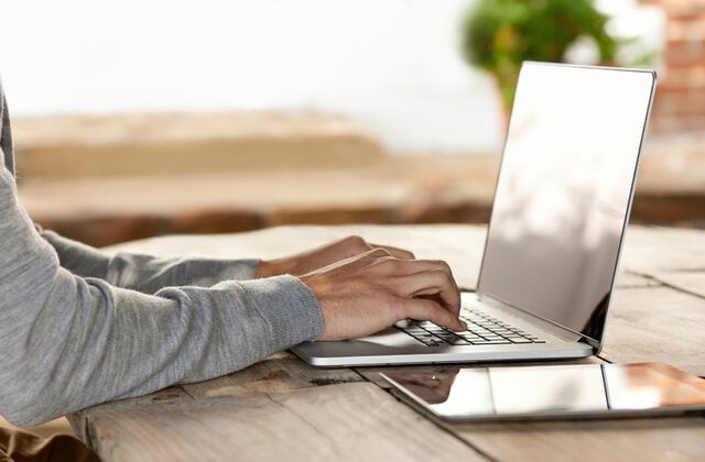 person wearing ash sweater using laptop on grey table