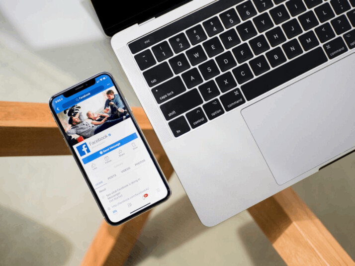 An iPhone X with the Facebook app opened is placed beside a MacBook.