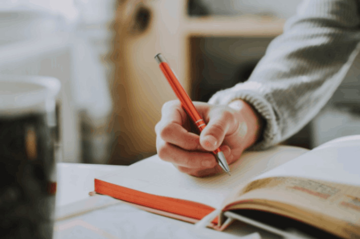 person holding on red pen while writing on book