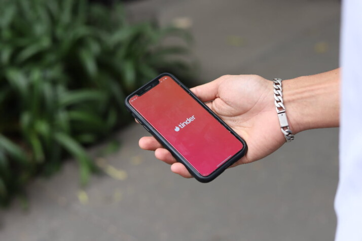 A person holding a phone with the tinder logo on the screen.