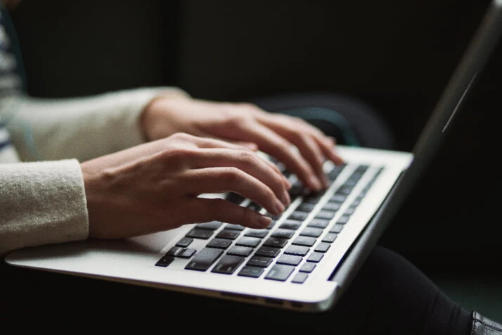 A lady with a laptop on her lap is typing on the keyboard.