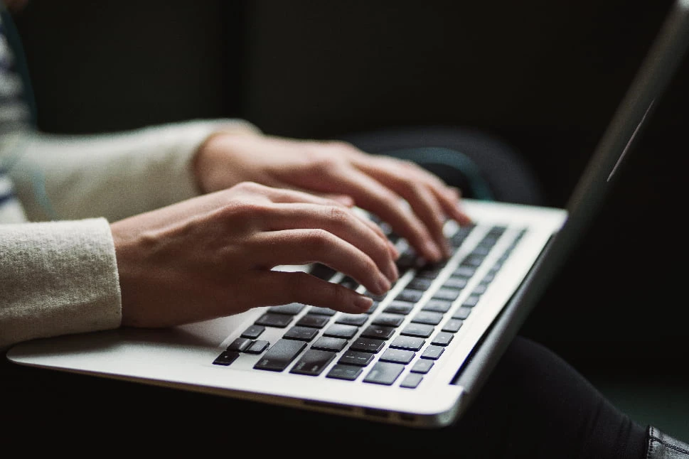 A lady with a laptop on her lap is typing on the keyboard.