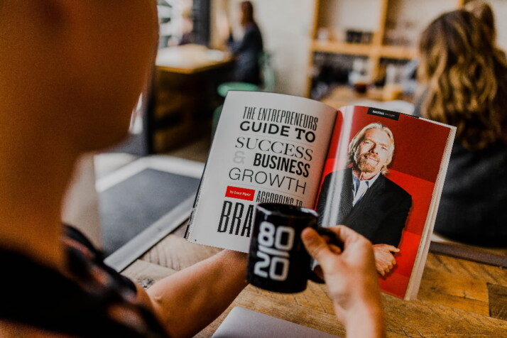 A person reading a magazine while drinking a cup of coffee.