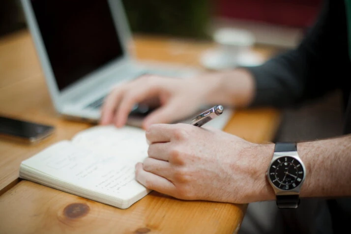 A person wearing a watch writing something on a notebook.