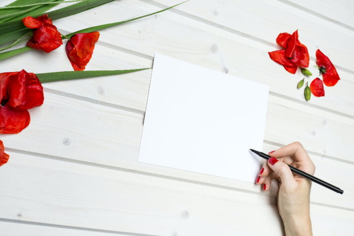 A person writing on a blank paper with rose petals surrounding it.
