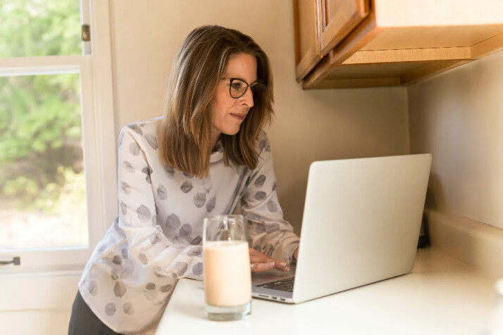 A woman working on her laptop with a glass of milk next to her.