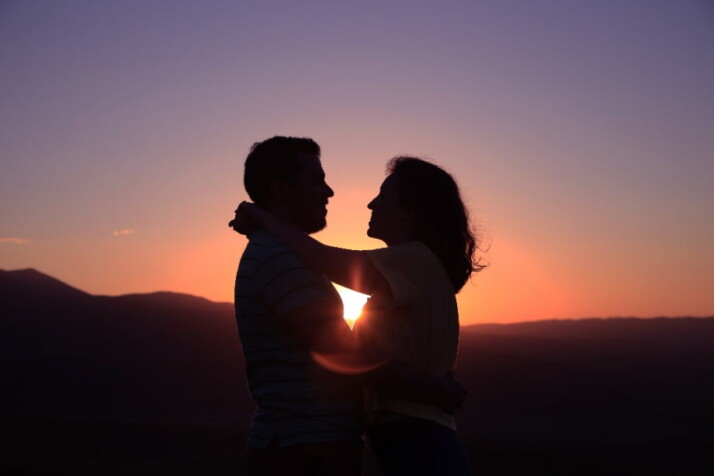 A photo of a couple facing each other with the sunset as a background.