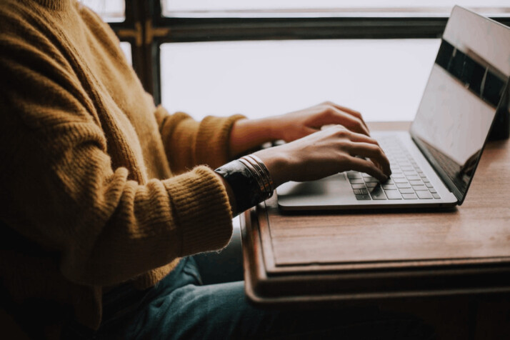 person wearing yellow sweater and blue jean sitting front of laptop