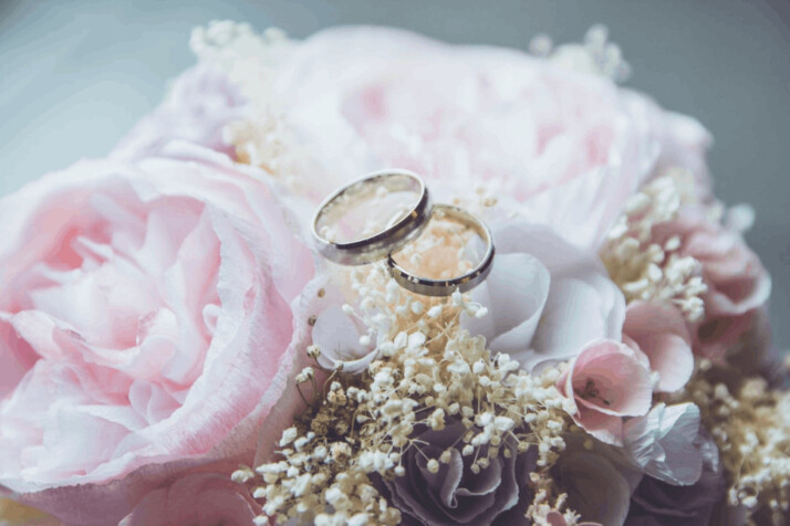 Gold-colored bridal ring set on pink rose flower bouquet