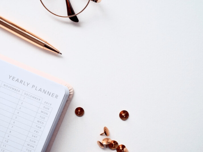 Buttons and thumbtacks beside planner book on white table