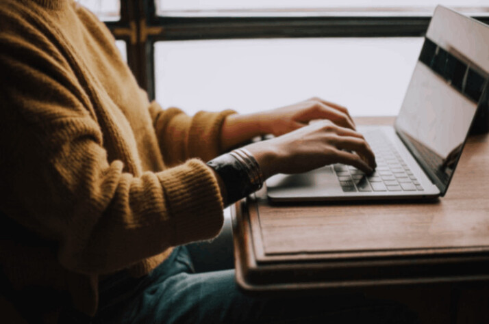 person wearing yellow sweater and jean trousers sitting in front of laptop