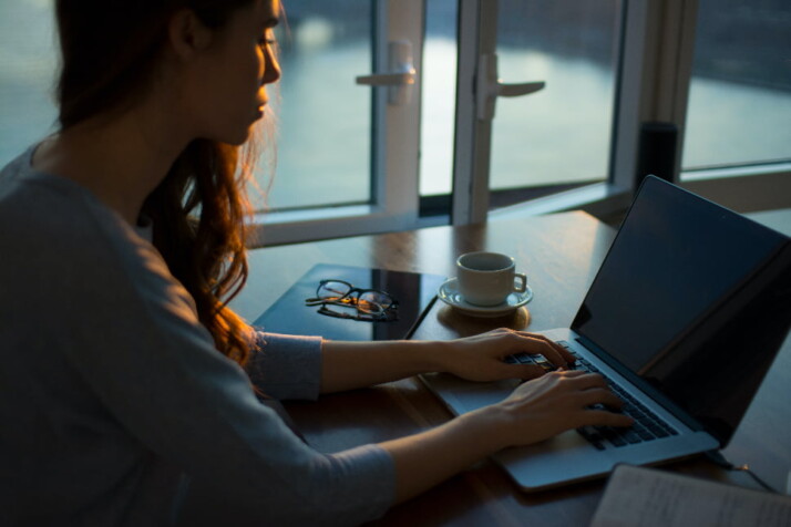 A woman typing on her laptop with a cup of coffee on the table.