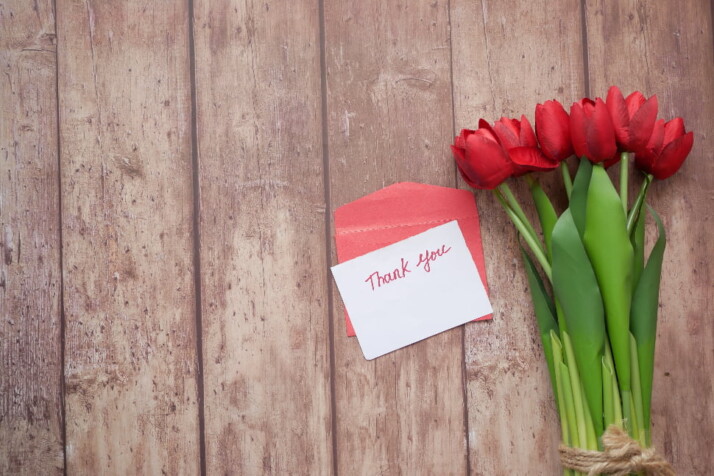 A thank you note on a red envelope with some roses next to it.