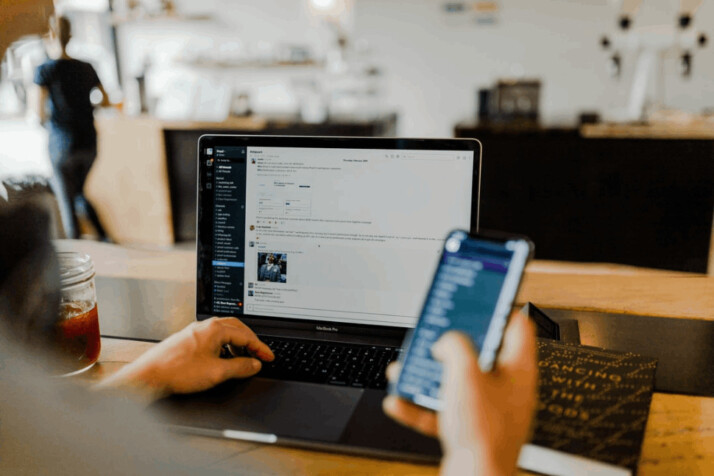 A person using a phone and a laptop in the office. 