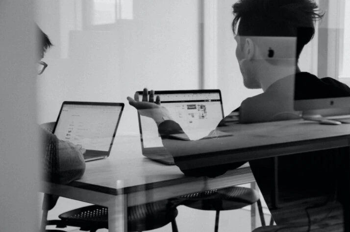 two men using MacBook on white table in room