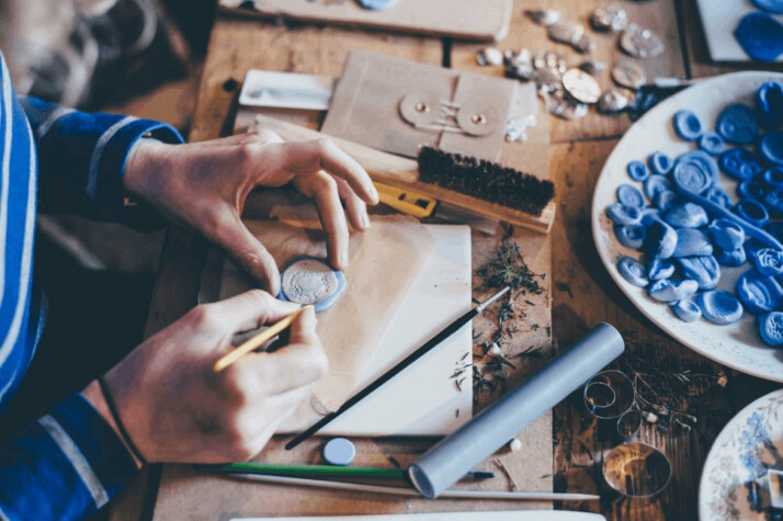 table filled with handcraft tools and person making handcrafts