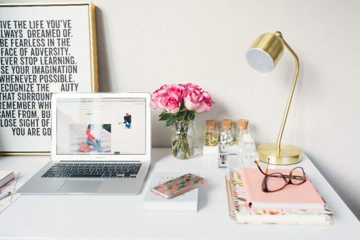 A neat work station with a laptop, lamp, flowers, notebook, etc.