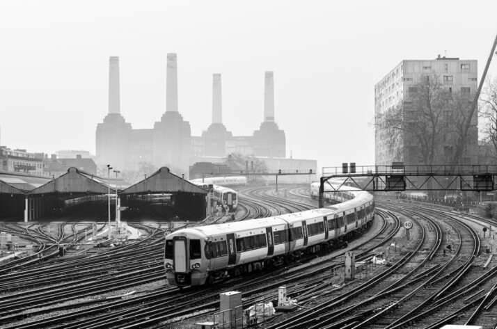 grayscale photo of train on rail tracks near non working factories.