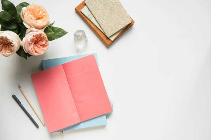 A pink open notebook placed on a table next to pink roses.