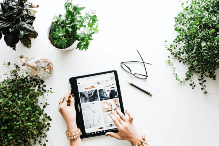 person using black tablet computer on a white surface with plants and shrubs around