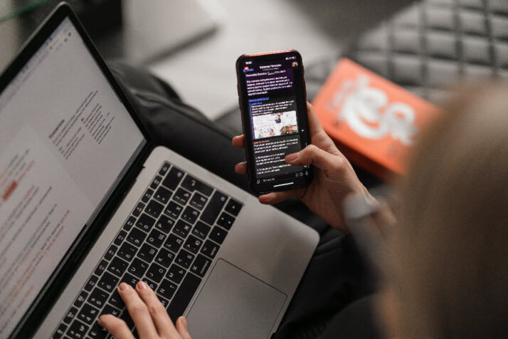 Young woman on a leather couch working aa laptop while browsing her phone.