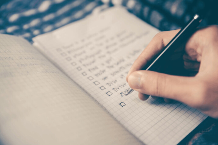 A person writing a bucket list on a notebook