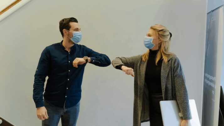 woman in black jacket holding white paper wearing a surgical mask.