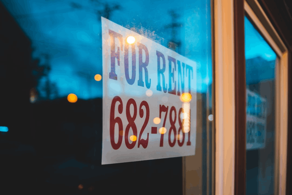 A red and blue signage pasted on a glass door for renting property