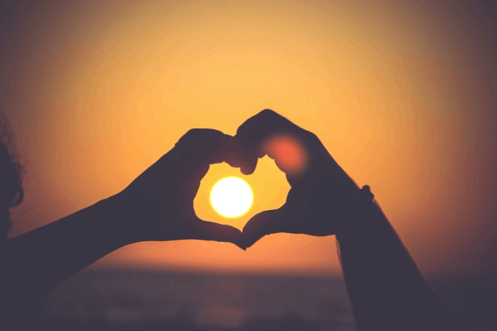 silhouette of person's hands forming heart over the shadow of the moon