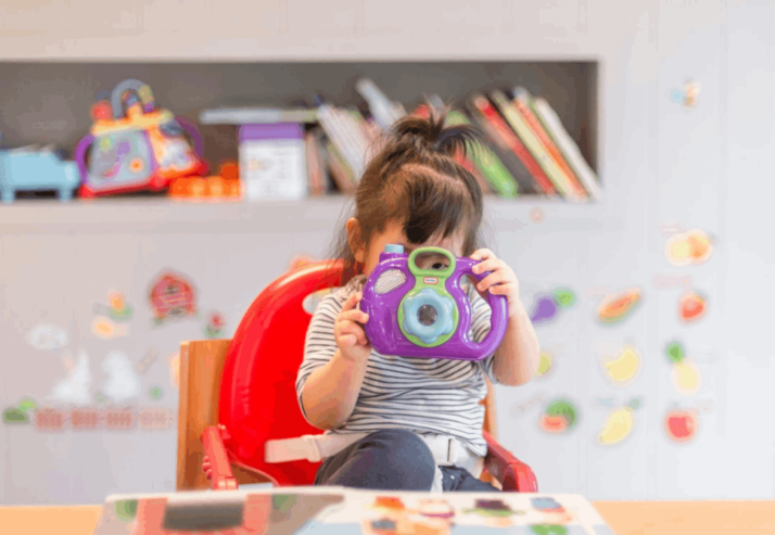 A little girl holding a purple and green camera toy