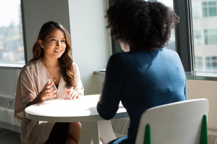 Two women talking while sitting across from each other on a round table.