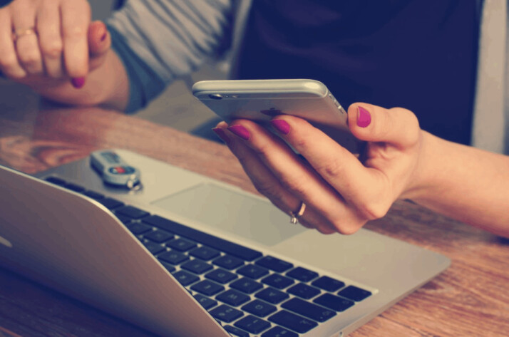 A woman holding a silver iPhone 6 in front of a laptop