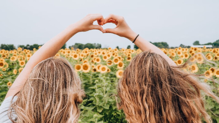 Two girls forming a heart with their hands while in a sunflower field.