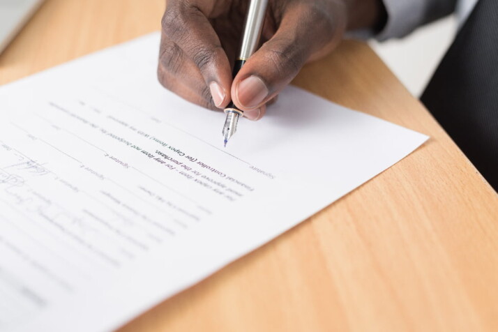 A person holding a pen and signing a contract.