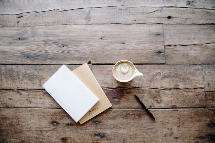 A cup of coffee with a heart foam on top next to a blank card.