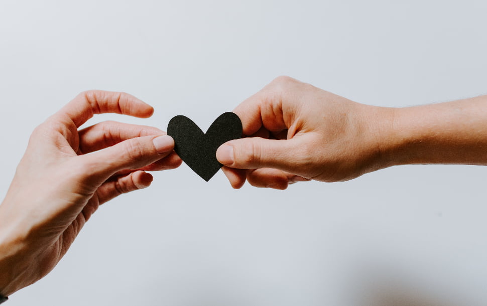 Two hands that are holding onto a black heart cut-out.