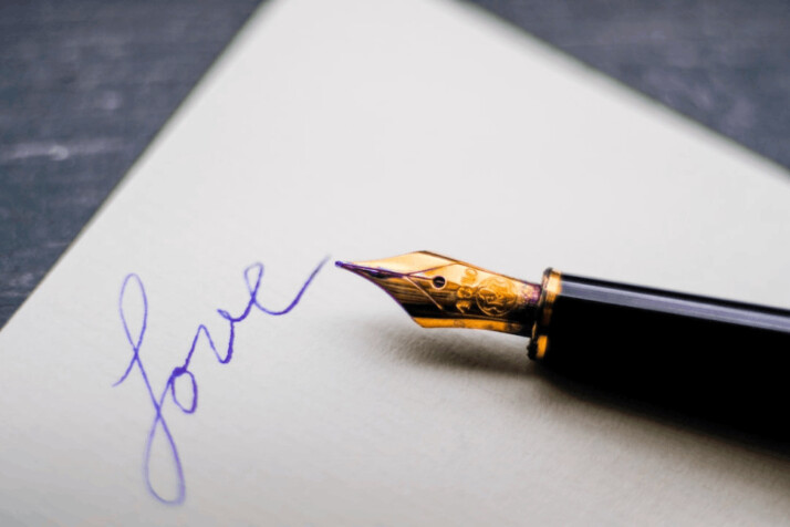 A black fountain pen on a white paper with the word Love