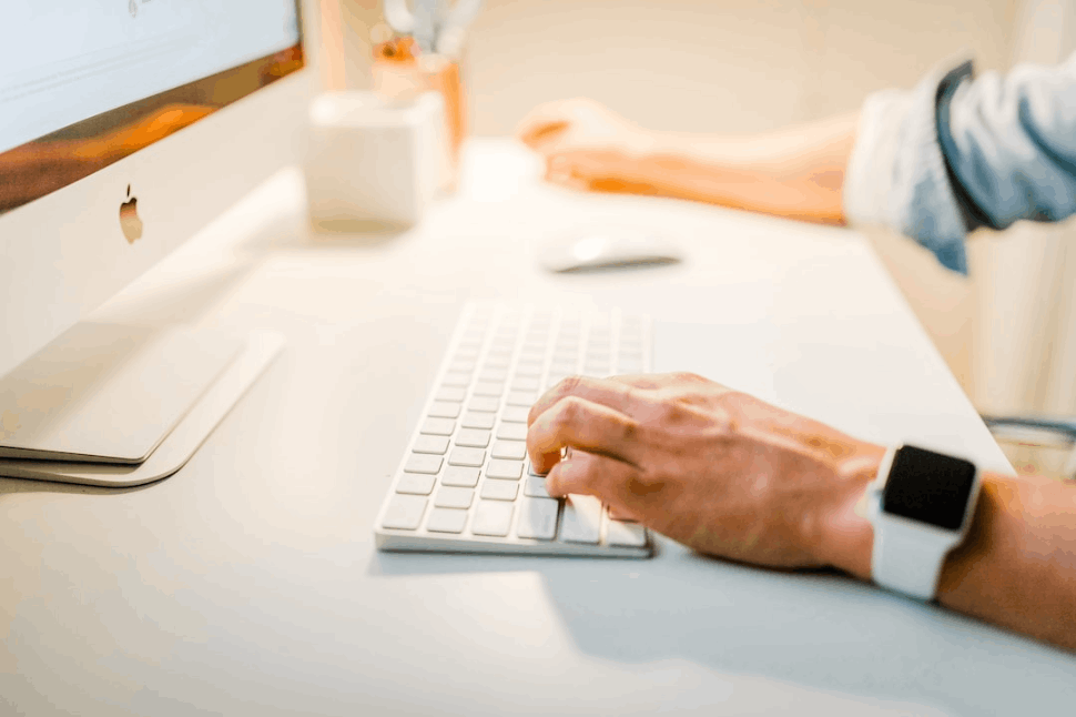 person wearing iWatch and blue shirt using iMac on white table