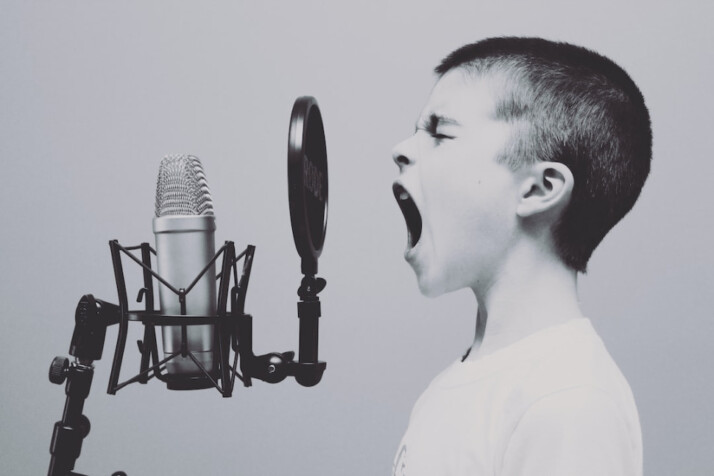 boy wearing white shirt singing on microphone with pop filter