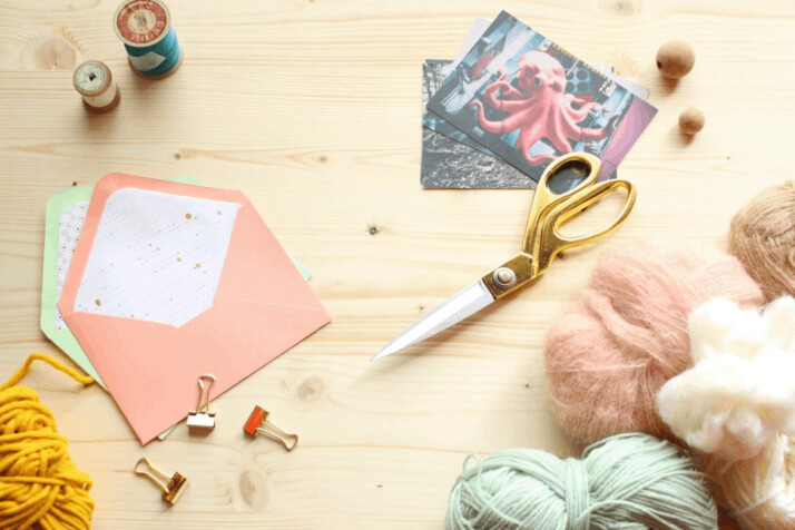Wool yarn, scissor, and envelopes are placed on a wooden table.