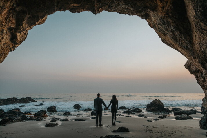 A couple holding hands pictured against the beautiful sky and ocean.