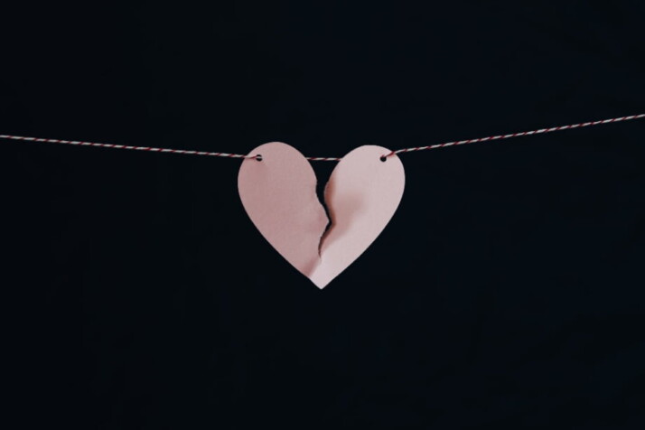 A heart cut-out hanging on a thread with a tear in the middle.