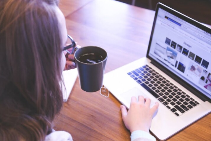 A woman drinking a cup of tea while browsing on her laptop.