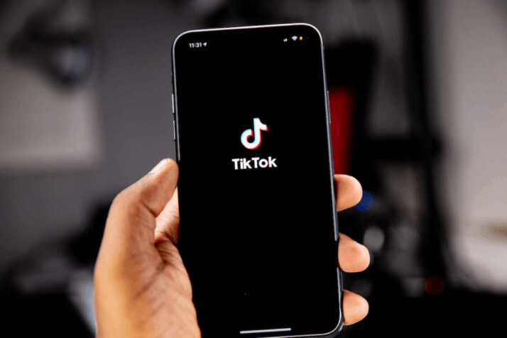 person holding black iphone that has the tiktok mobile app opening screen.
