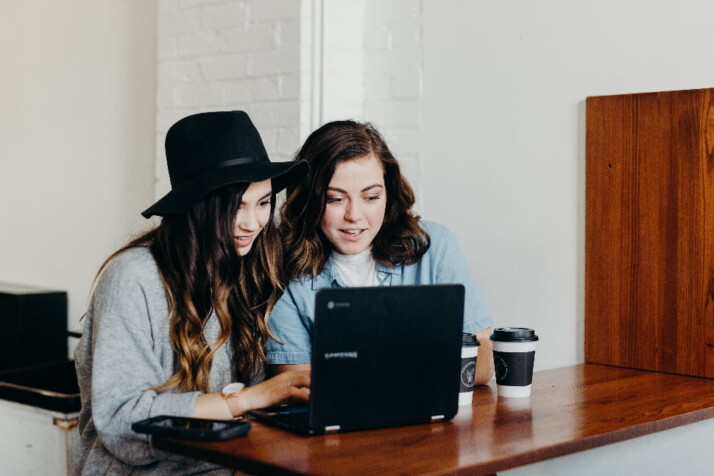 Two teens sitting beside each other, working a laptop.