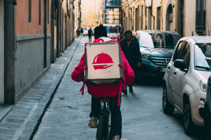 delivery man wearing red jacket and jean riding a bicycle