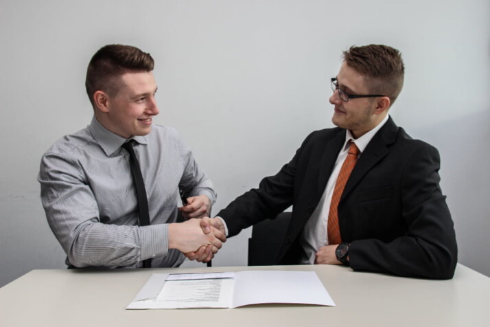 Two men smiling, sealing a deal with a handshake.