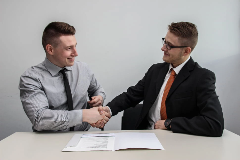 Two men smiling, sealing a deal with a handshake.