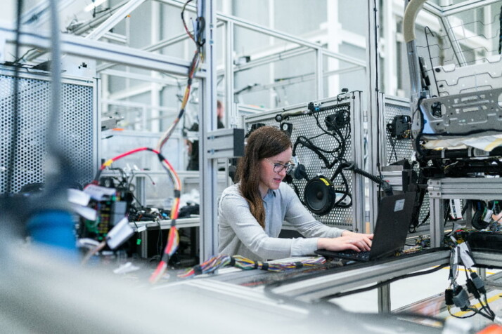 A woman engineer sitting in her work station surrounded by wires and devices.